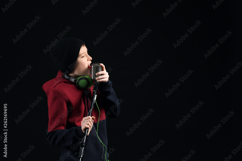 Teenage boy with microphone singing against dark background