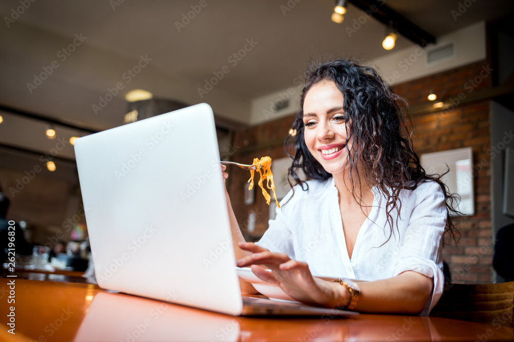 Latin young woman working on laptop computer at restaurant, eating break during work