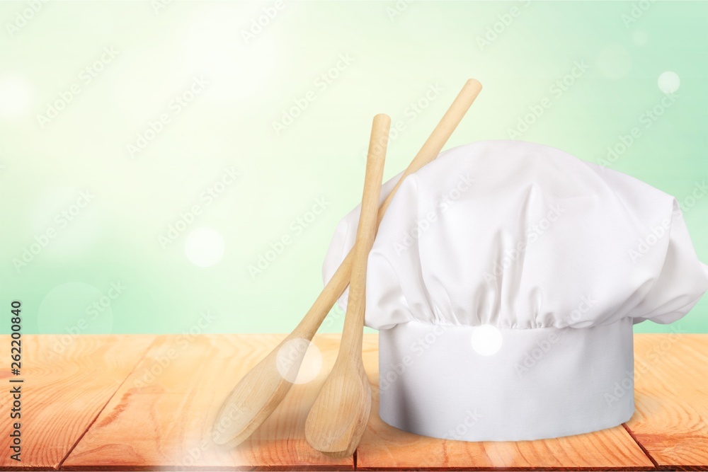 White cooks cap and wooden spoons on wooden table