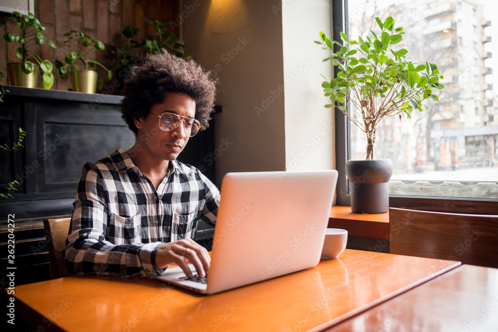 African man in glasses using laptop while sitting at restaurant, concept of young people working