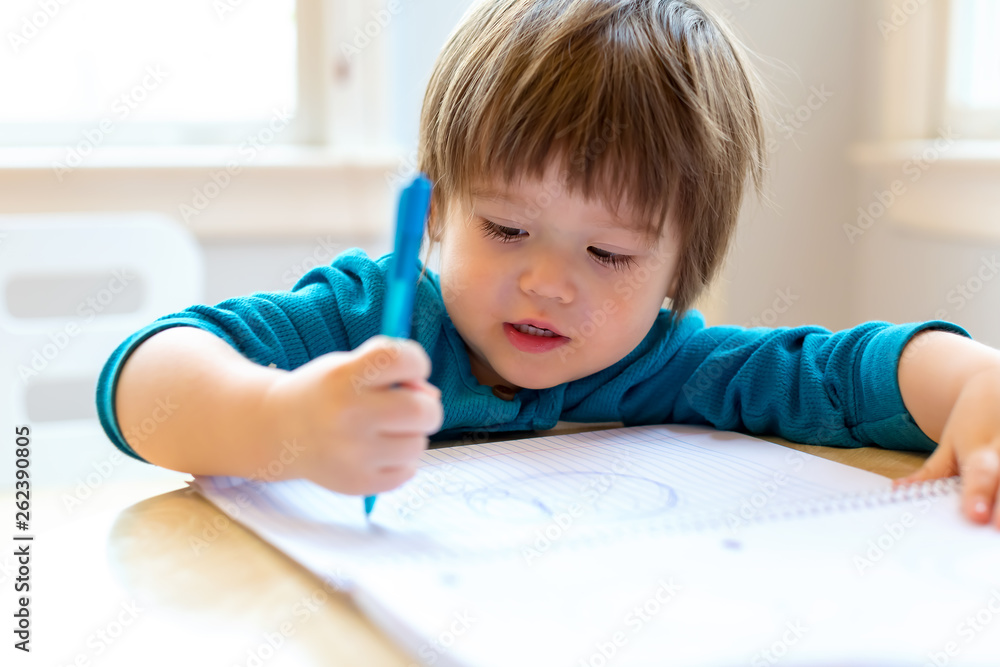 Toddler boy drawing with pen and paper at his desk