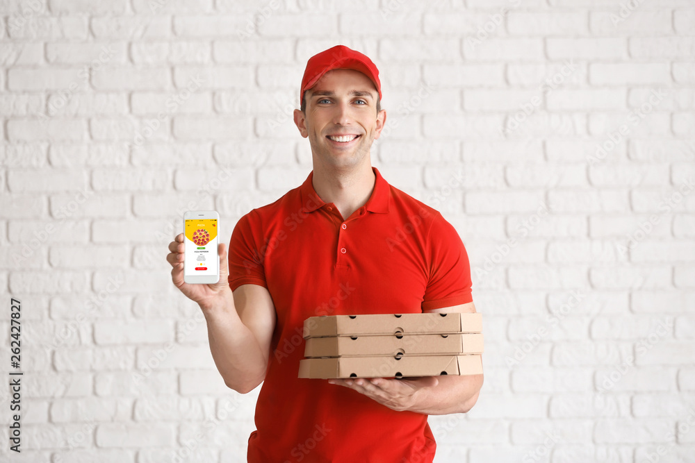 Young man with pizza boxes and mobile phone near white brick wall. Food delivery service