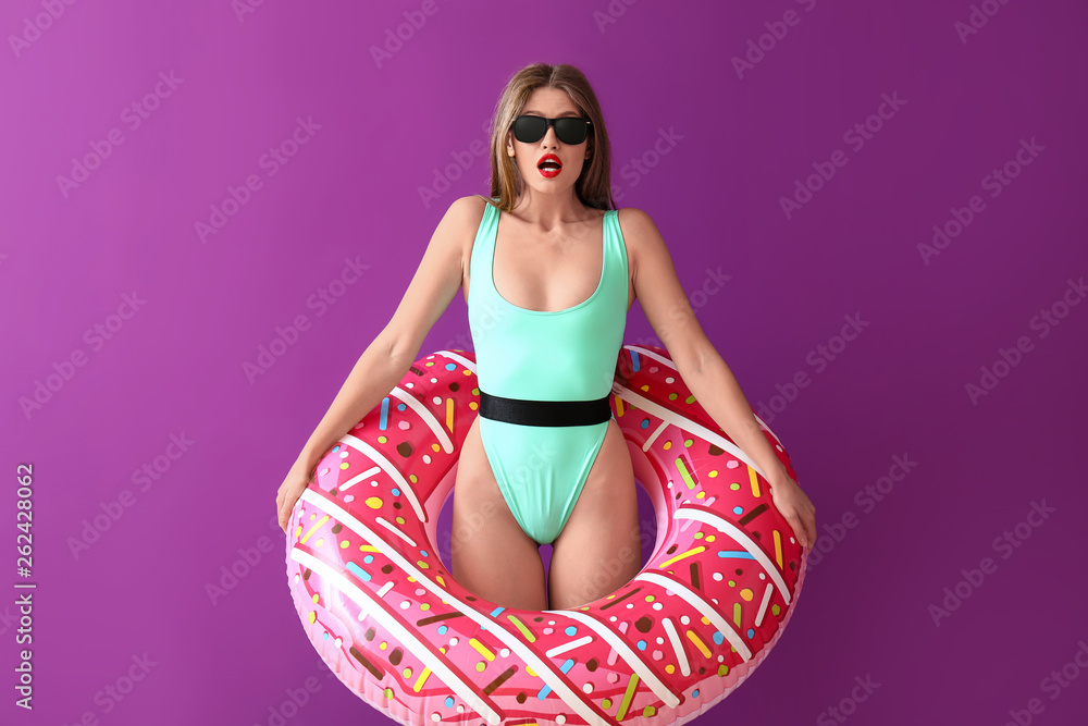 Surprised young woman with inflatable ring on color background