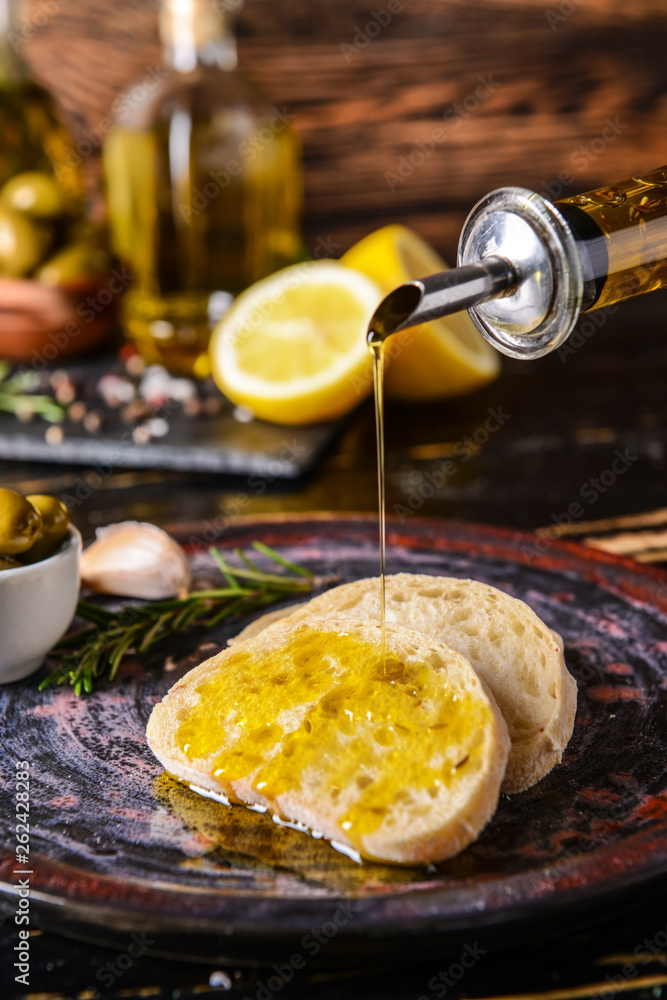 Pouring of tasty olive oil from bottle onto fresh bread