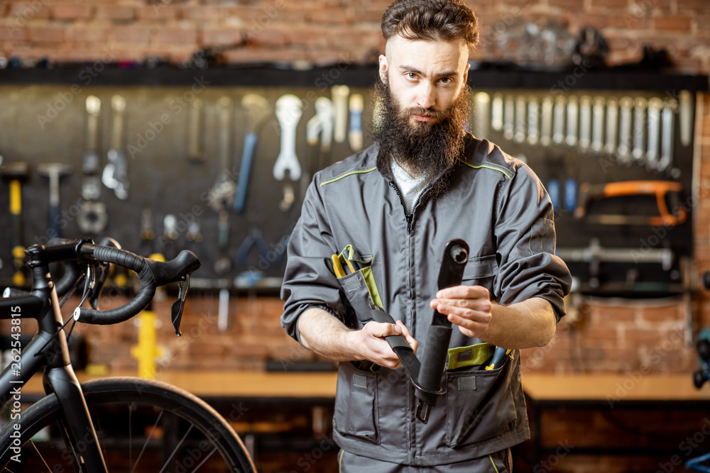 Portrait of a handsome bearded repairman in workwear standing with wrenches at the bicycle workshop