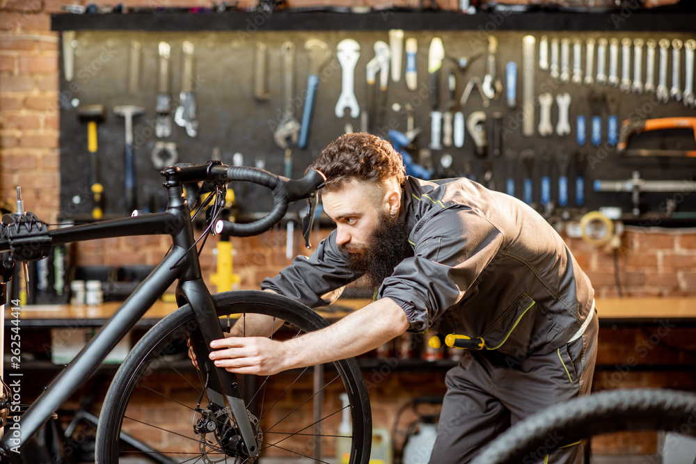 Handsome bearded repairman in workwear serving a sports bike at the bicycle workshop