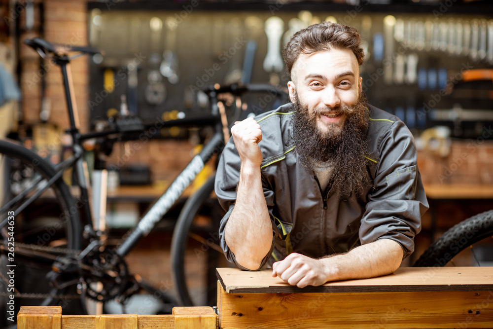 Portrait of a handsome cheerful repairman in workwear at the bicycle workshop