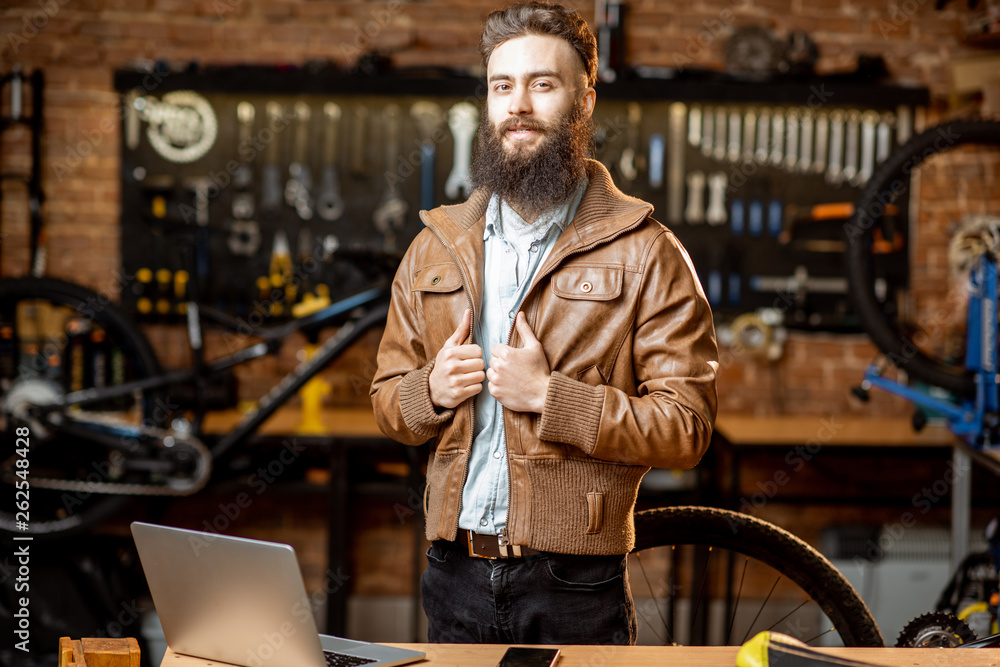 Portrait of a handsome bearded man as bicycle store owner or manager standing with laptop at the bic