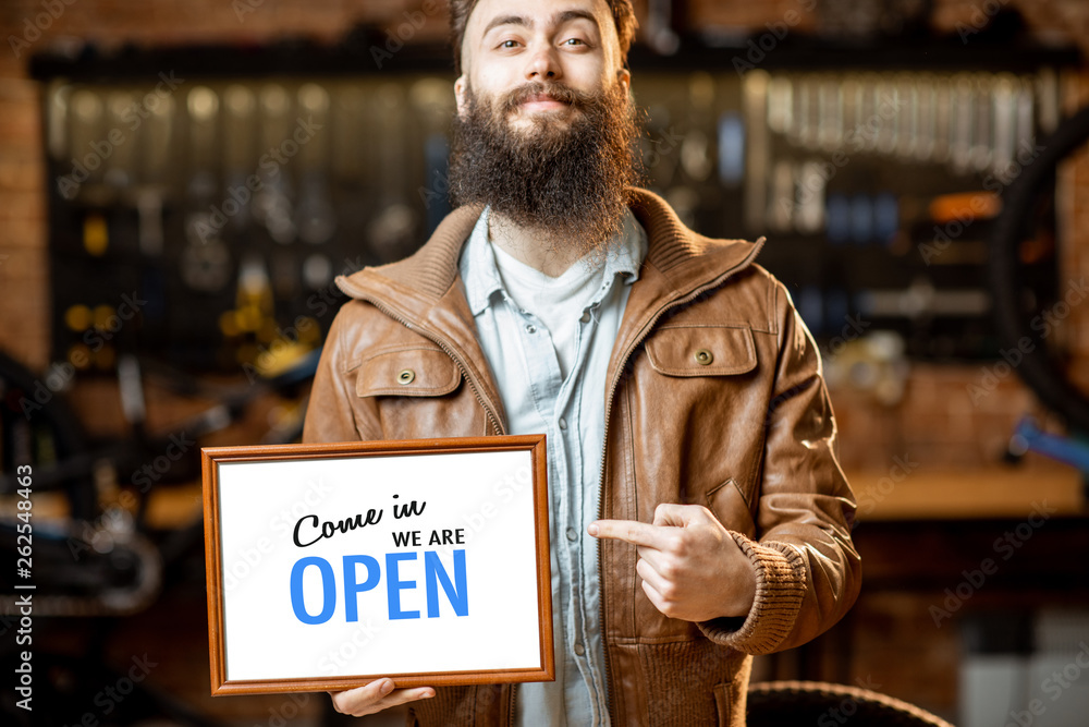 Stylish man as a shop owner or manager standing with welcome plate in the bicycle workshop