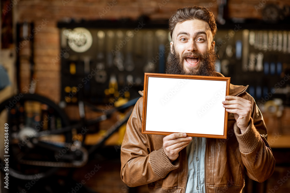 Stylish man as a shop owner or manager standing with blank plate in the bicycle workshop