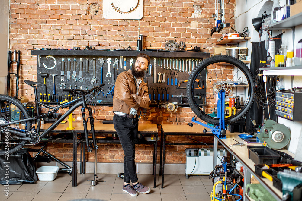 Portrait of a young stylish businessman as a shop owner standing at the bicycle workshop