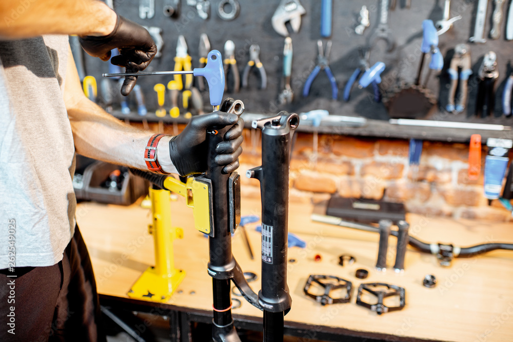 Man disassembling shock absorber of a bicycle fork at the workshop, close-up view