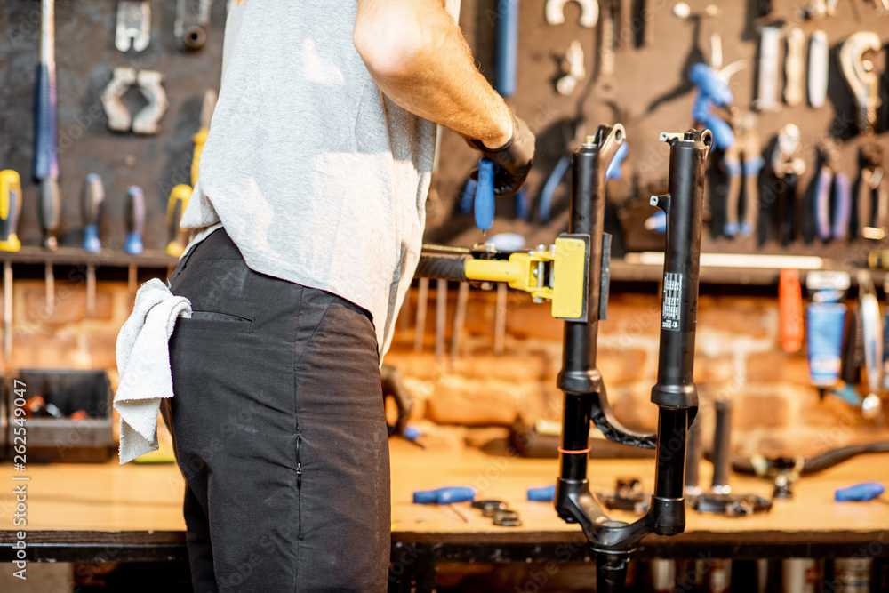 Man disassembling shock absorber of a bicycle fork at the workshop, close-up view