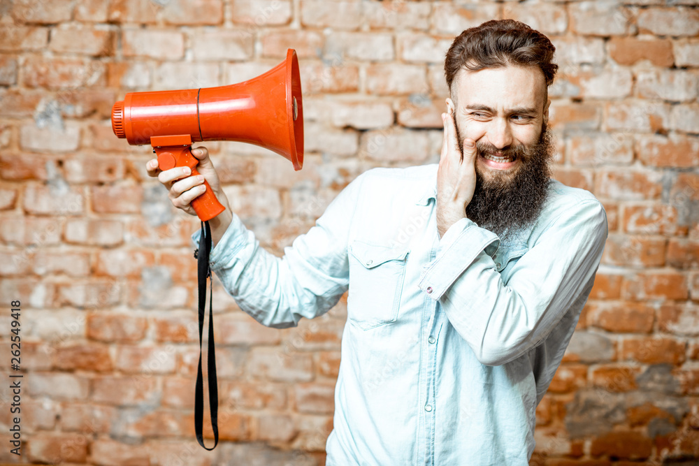 Handsome bearded man with red loudspeaker on the brick wall background