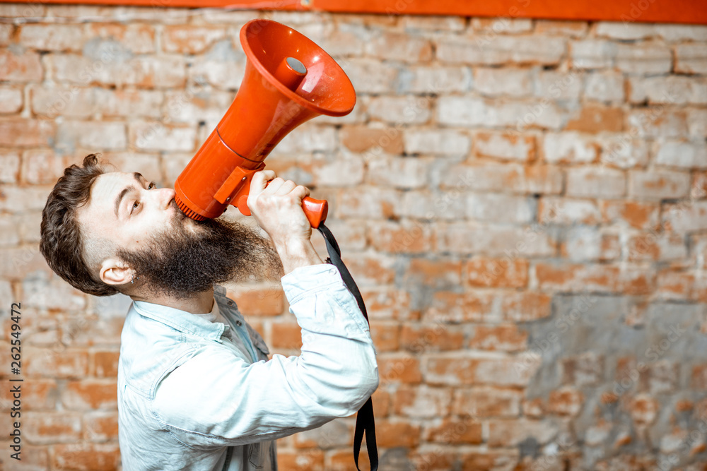 Handsome bearded man with red loudspeaker on the brick wall background