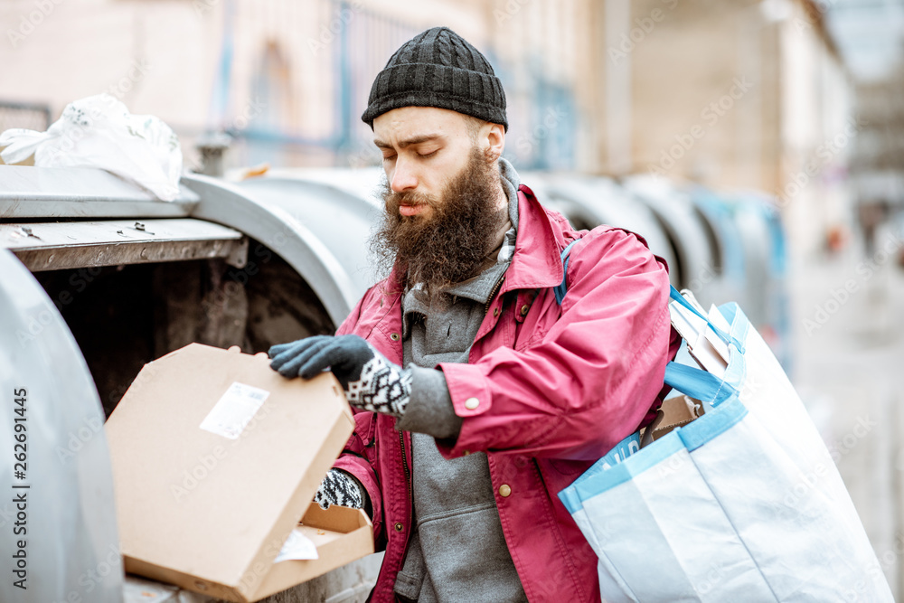 Homeless bearded beggar searching some food, rummaging in the trash in the city. Concept of poverty 