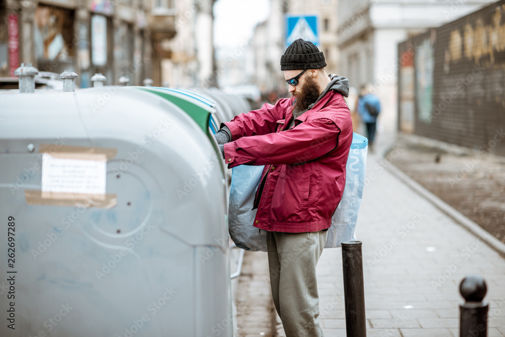 Homeless stylish beggar searching some food or valuable things in the trash containers in the old ci