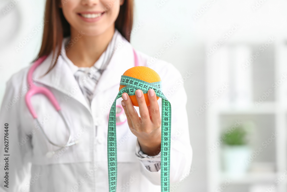 Female nutritionist with orange and measuring tape, closeup