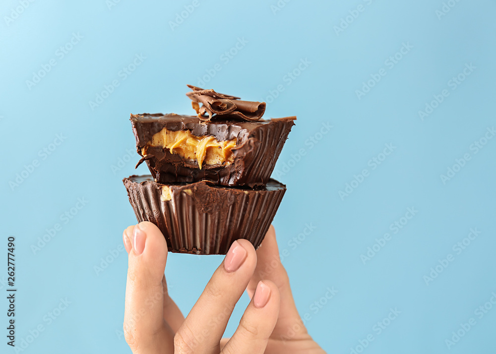 Female hand with chocolate butter cups on color background