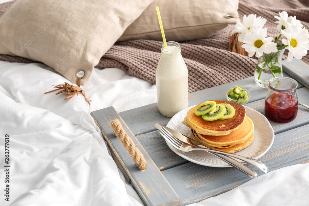 Tray with tasty breakfast and flowers on bed