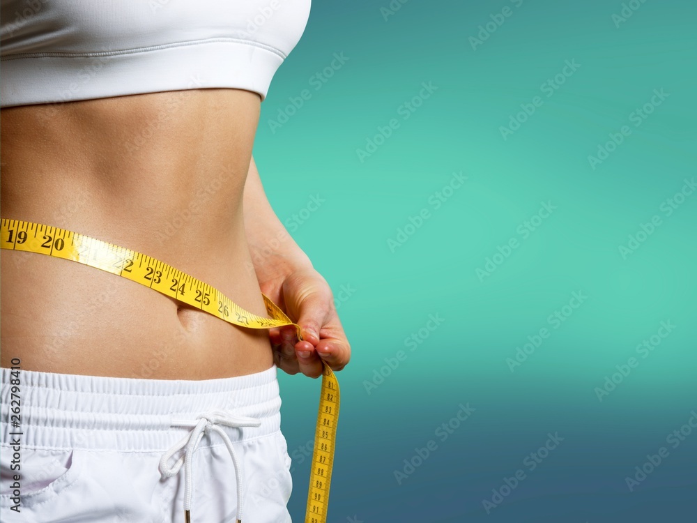 Slim young woman measuring her thin waist with a tape measure, close up