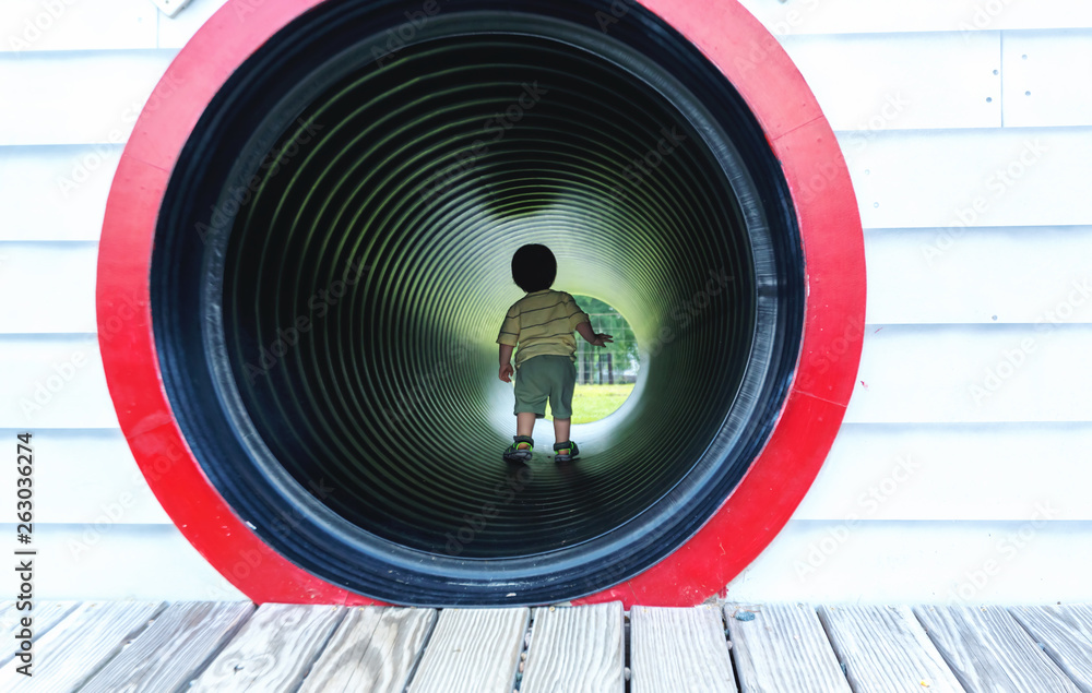 Toddler boy playing in a tunnel at a playground