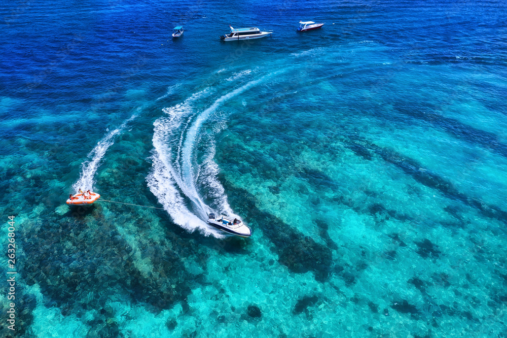 Yachts at the sea in Bali, Indonesia. Aerial view of luxury floating boat on transparent turquoise w