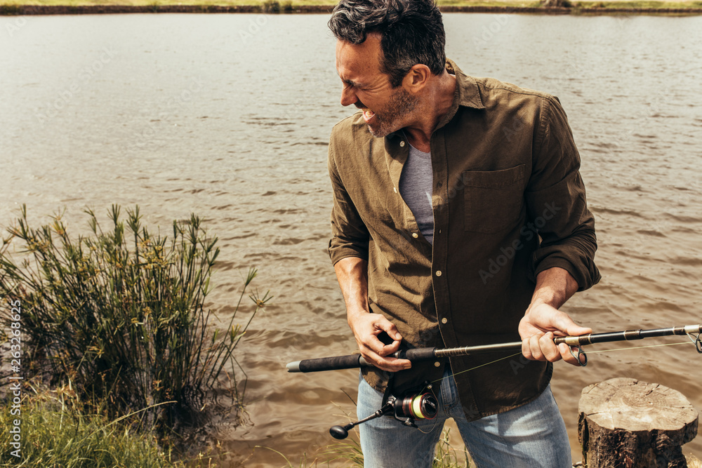 Portrait of a man standing near a lake holding a fishing rod