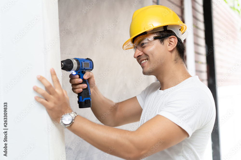 Man in helmet with electric drill making hole in wall Architecture and Home renovation concept.