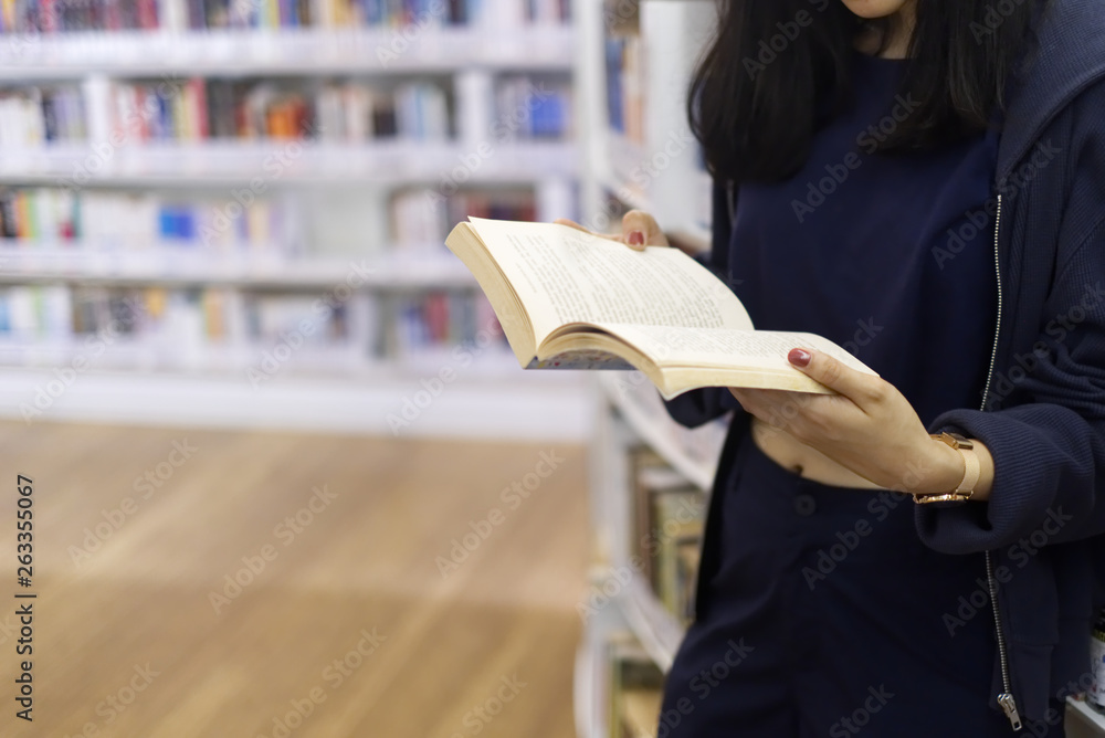 年轻女孩站在图书馆看书的裁剪镜头。她双手拿着打开的书