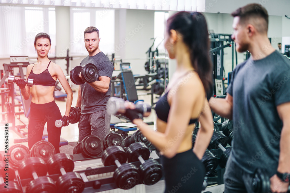 Beautiful girl and strong man with metal dumbbells looking at their reflection in the mirror. Person