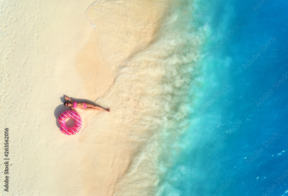 Aerial view of the beautiful young lying woman with pink donut swim ring on the white sandy beach ne