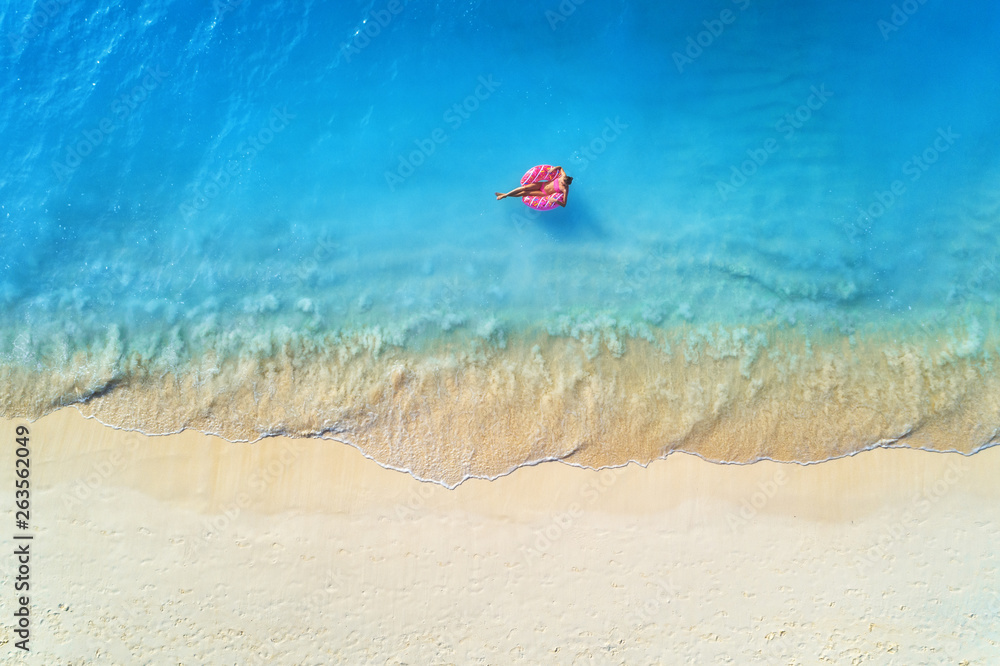 Aerial view of a young woman swimming with the donut swim ring in the clear blue sea with waves at s