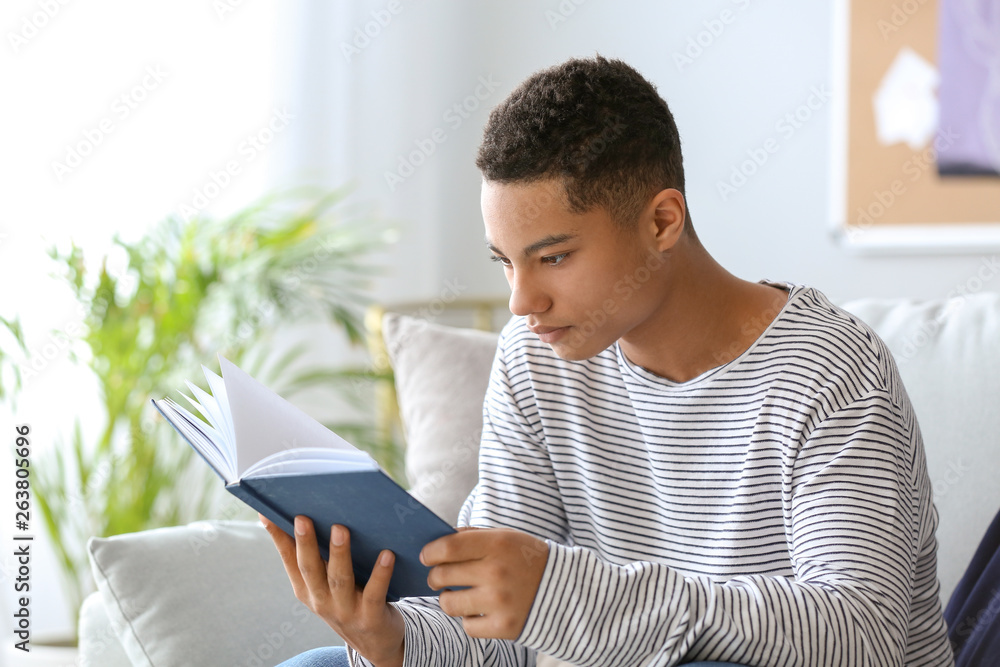 African-American teenage boy reading book at home