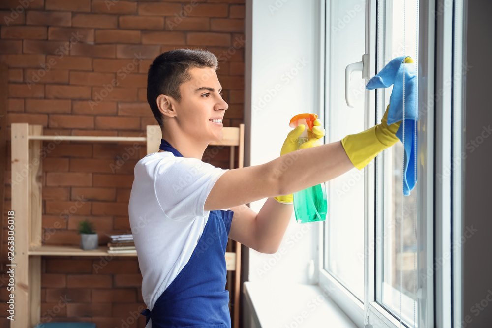 Male janitor cleaning window in office