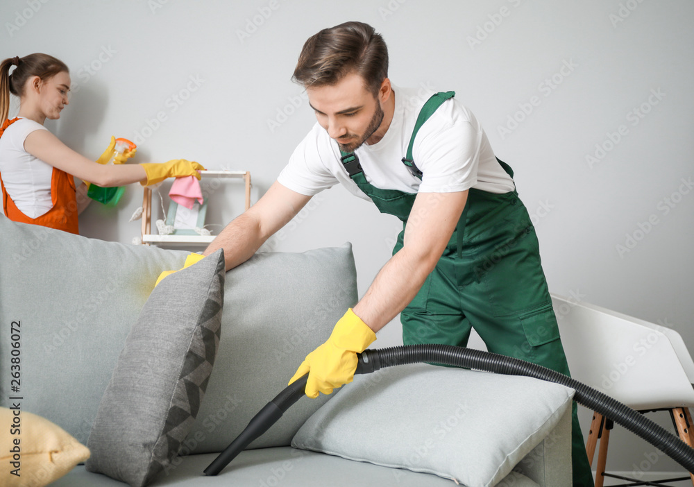 Male janitor cleaning sofa in room