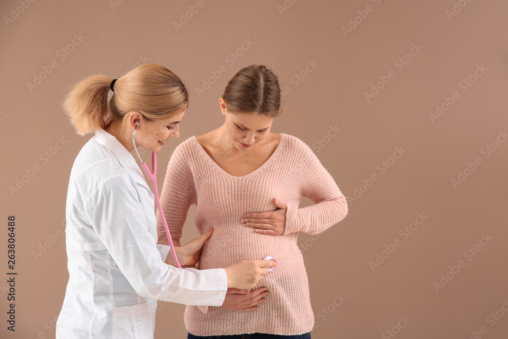 Gynecologist examining young pregnant woman on color background