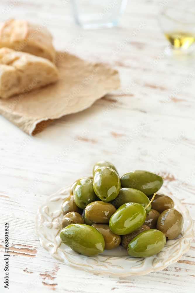 Plate with tasty olives on white table