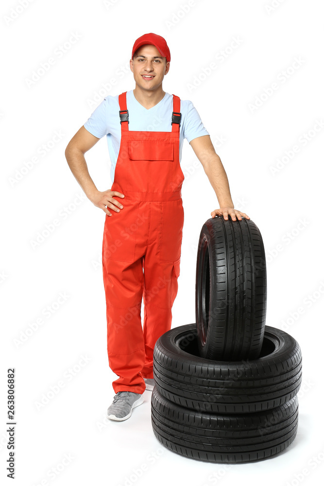 Young male mechanic in uniform with car tires on white background