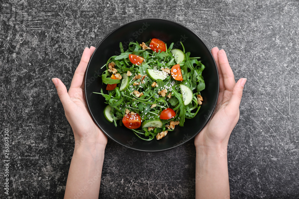 Female hands holding plate with tasty arugula salad on grey background