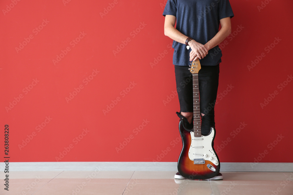 Handsome young man with guitar near color wall