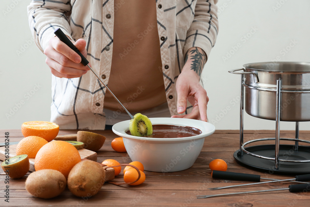 Woman dipping fresh kiwi into chocolate fondue at table