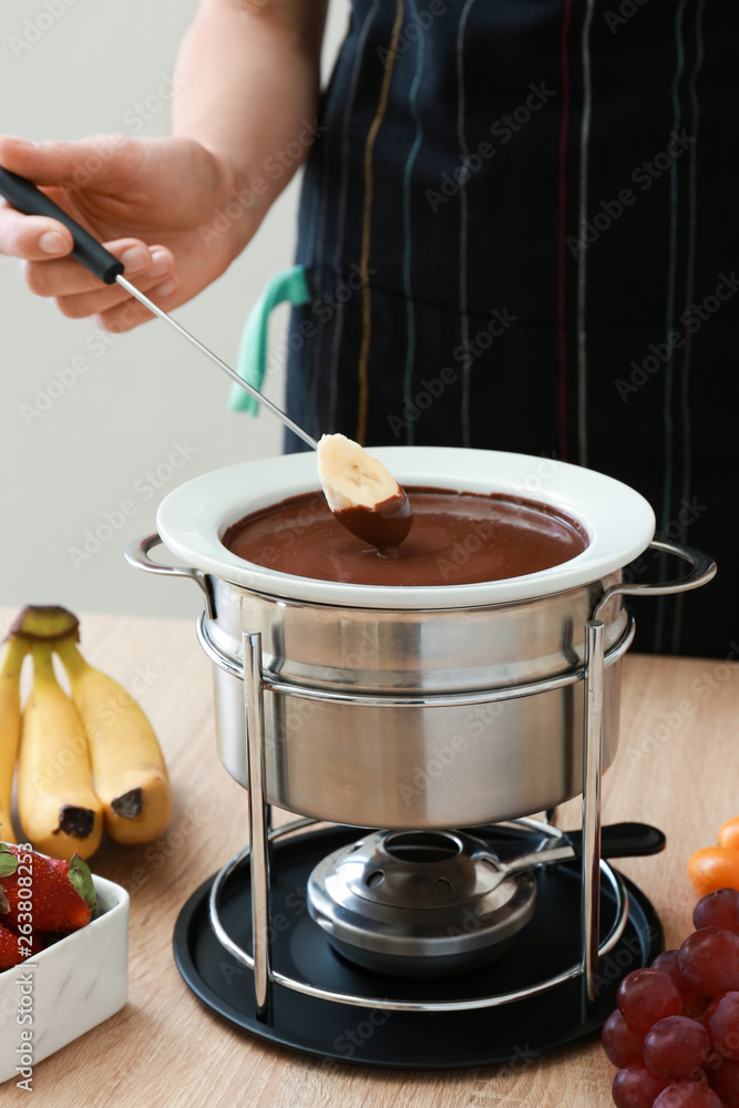 Woman dipping fresh banana into chocolate fondue at table