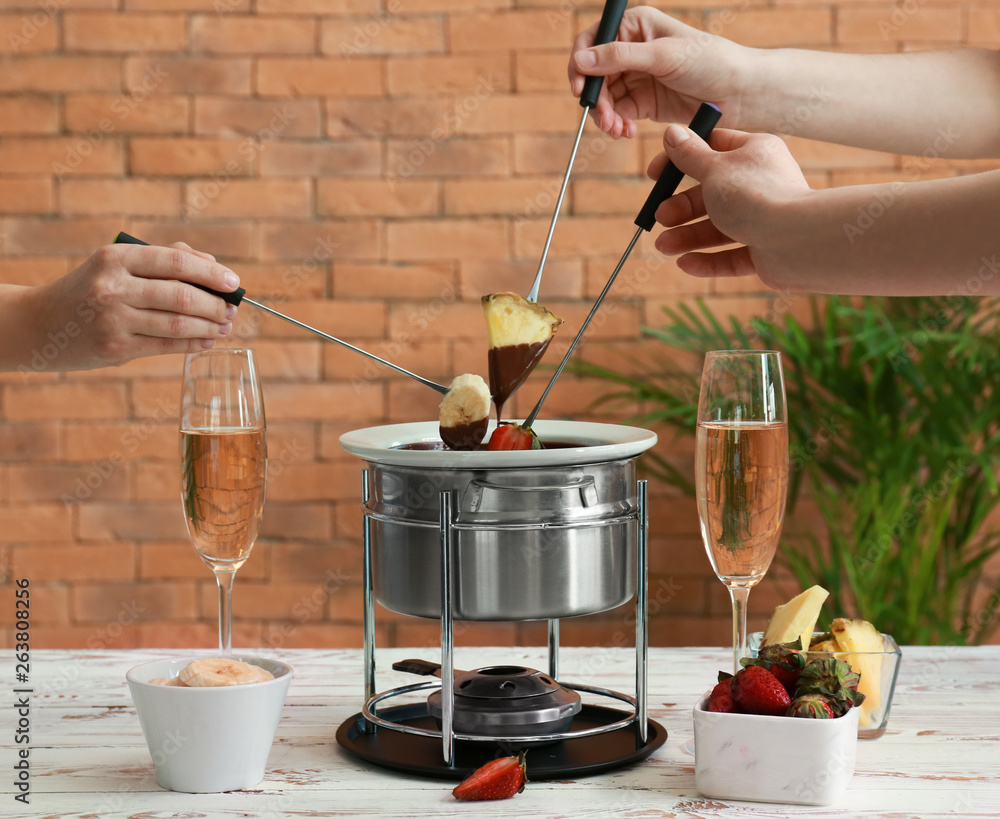 Women dipping fresh fruits into chocolate fondue