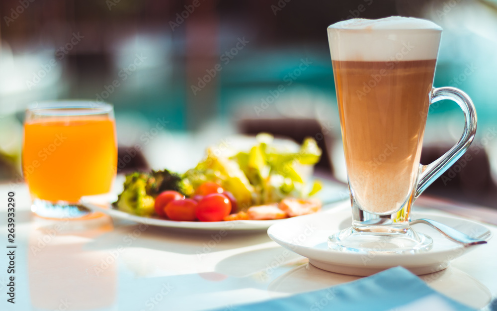 Tall glass of latter coffee on a table in ourdoor area next to swimming pool, hot drink and breakfas