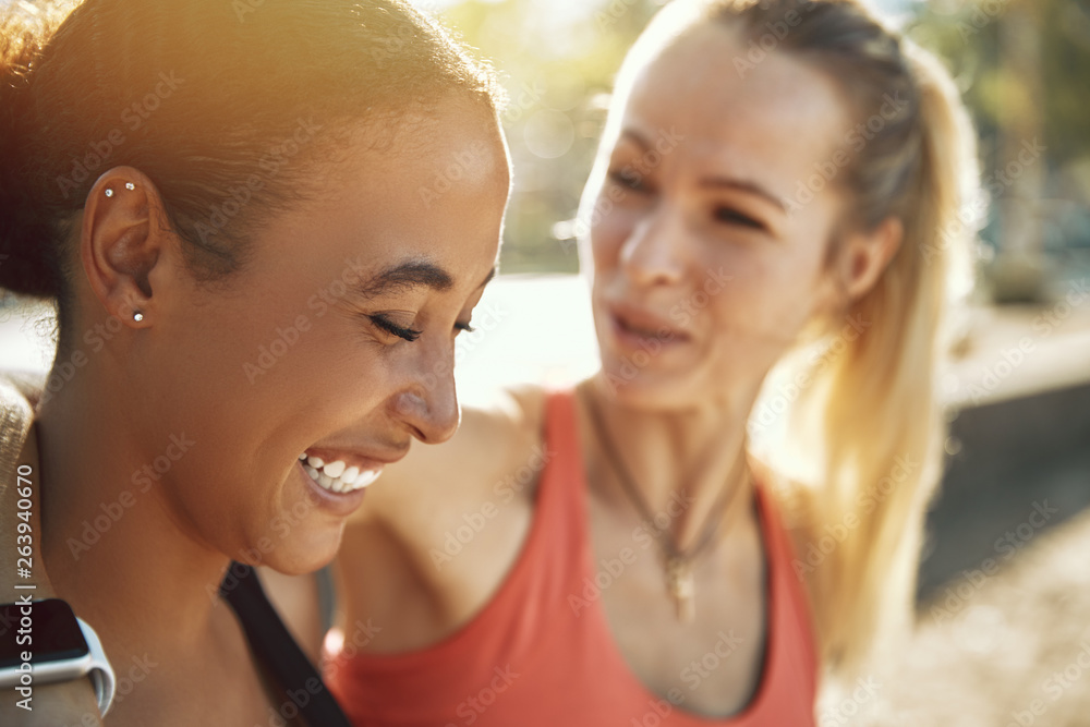 Fit women laughing while standing outside on a sunny day