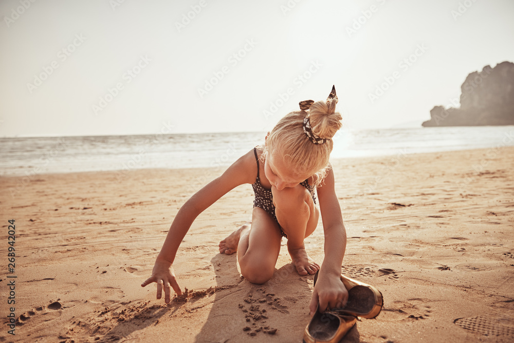 Cute little girl drawing in the sand on a beach