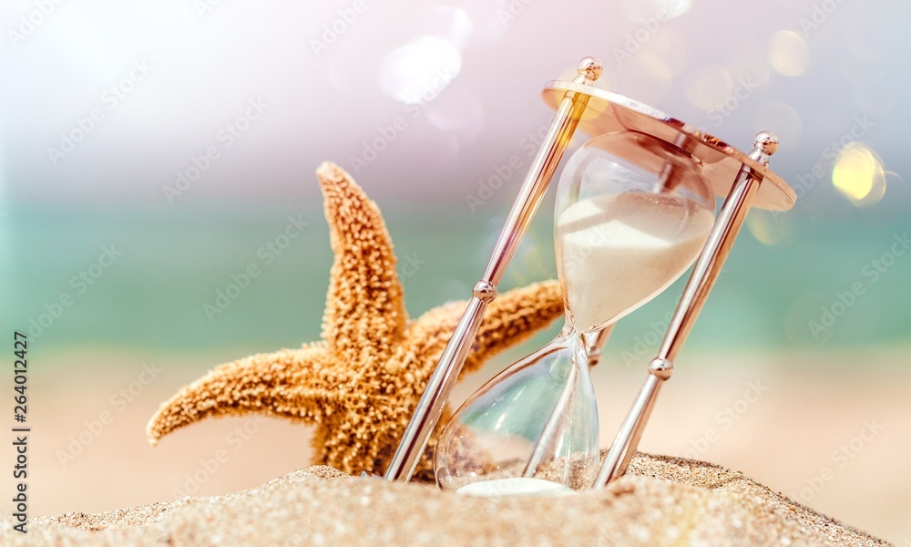 Hourglass and seastar on sandy beach