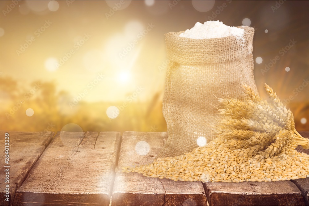 Wheat ears and flour on wooden desk on blurred field background