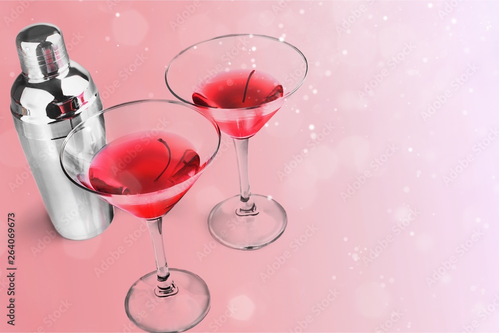 Glasses of red martini with cherries and silver shaker on white background